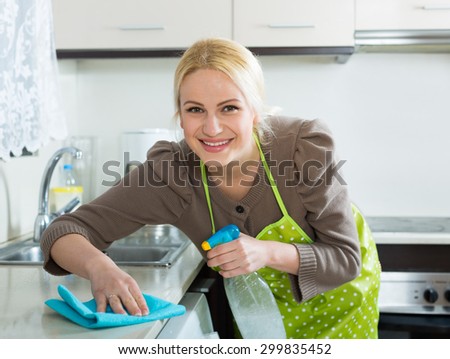 Happy girl cleaning furniture in kitchen in the home