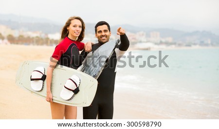 positive adult couple running on the beach with surf boards