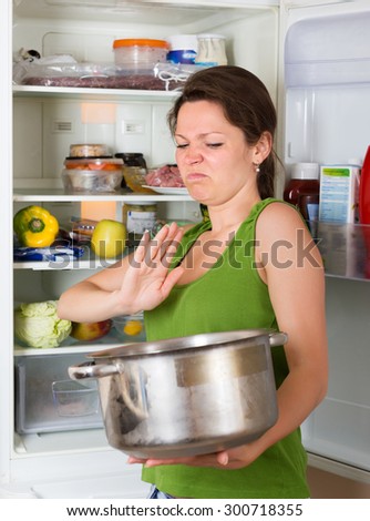 Woman holding her nose because of bad smell from food near refrigerator  at home