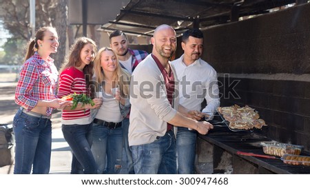 Positive smiling colleagues making grill at corporate party outdoor. Selective focus