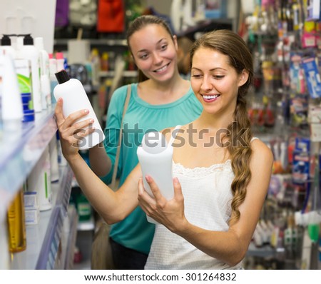 Two joyful smiling girls choosing shampoo at supermarket. Selective focus