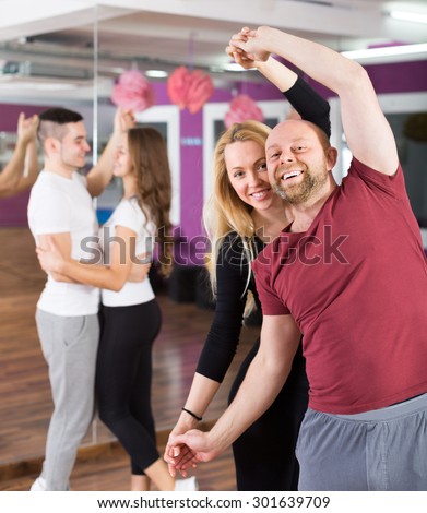 Group of cheerful smiling young adults dancing salsa in club. Focus on guy