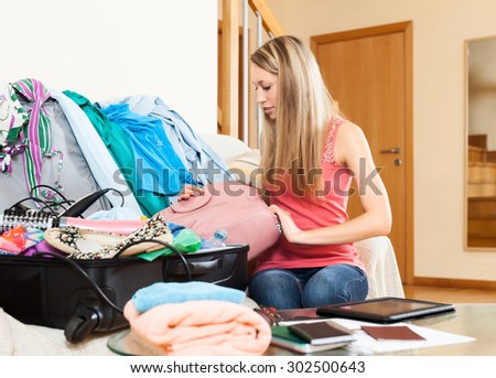 Serious woman with long hair packing clothes and accessories into suitcase