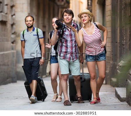 Company of active smiling travelers with travel bags walking the city