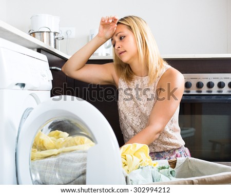 Home laundry. Tired girl using washing machine at home