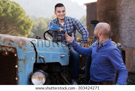 Two farmers talking near the agricultural machinery in the shed