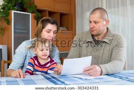 Worried family with child sitting at table with financial documents