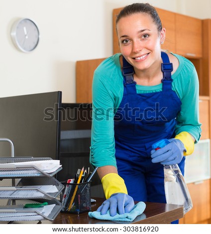 Smiling professional female cleaner in uniform cleaning at office with sprayer
