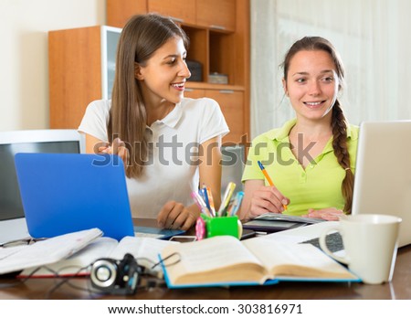 Two girls are studying at the table wit their textbooks and laptops in a living room
