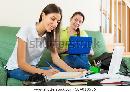 Smiling young student girls studying at home with books and computers
