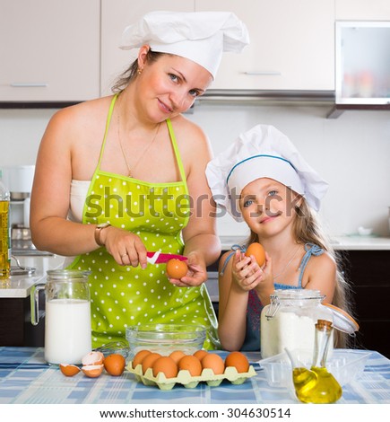 Smiling mother and her daughter in cap cooking omelette