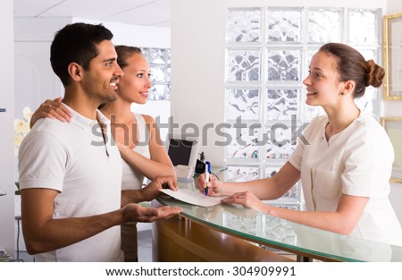 Positive young couple talking with secretary at reception in the clinic