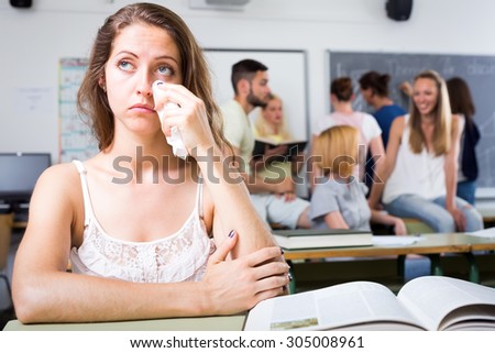 Sad crying girl sitting at her desk alone in college classroom