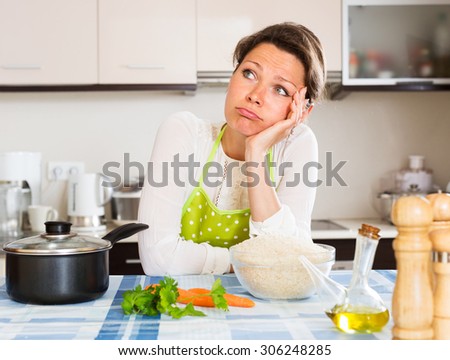 Pensive woman cooks rice with vegetables at home