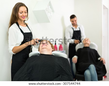 Portrait of an adult woman in a hairdressers salon. Her head is being washed by a young smiling hairdresser