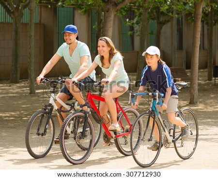 Smiling family of three cycling on street road in summer day
