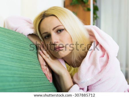 Sad and lonely woman in bathrobe sitting on couch at home