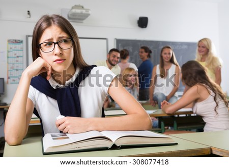 Alone american student being bullied by a group of students her chin on her hand
