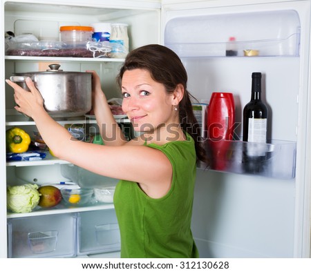 Hungry woman eating soup from pan near fridge  at kitchen