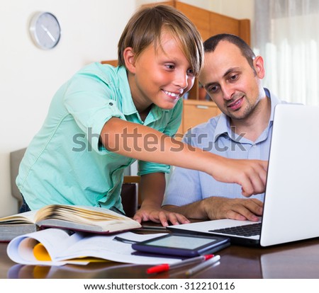 Positive man helping joyful teenage son to do homework at home