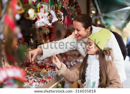Smiling mother with positive girl in Christmas market. Focus on girl