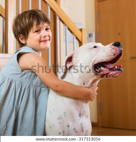 Happy smiling little girl hugging big white dog at home