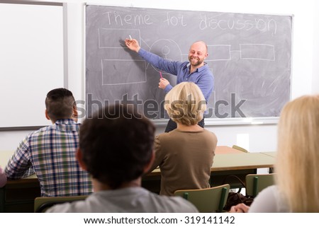 Professor standing at the chalk board in front of his students and showing them a diagram