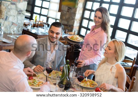 A company of people dining in a restaurant while smiling waitress is serving them