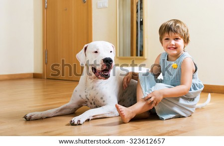 Positive smiling little girl with big white dog sitting on the floor at home