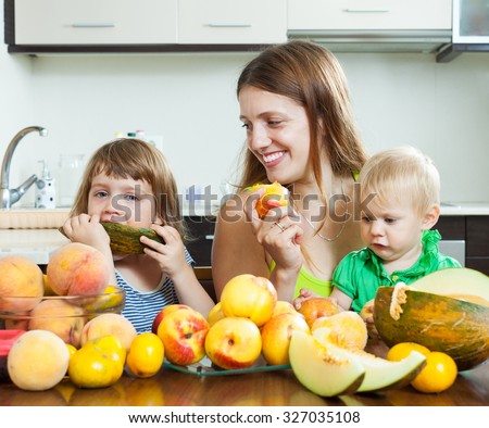 Happy woman with children eating melon and other fruits over  table at home interior