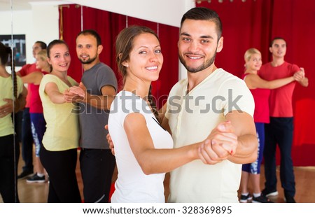 Happy smiling couple learning to dance waltz in dancing school with other dancing pairs in background