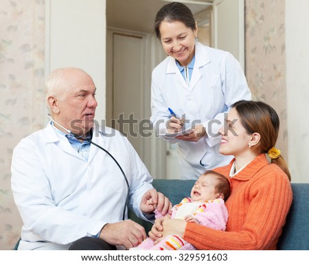 pediatrician doctor examining newborn baby on mother\'s arms in house. Mature nurse writes symptoms
