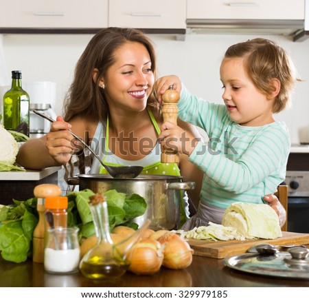 Positive young mother with little daughter cooking at home kitchen