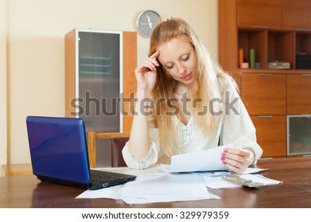 serious blonde woman reading financial documents at table in home