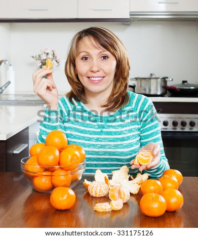 Smiling woman eating tangerines at table in home kitchen