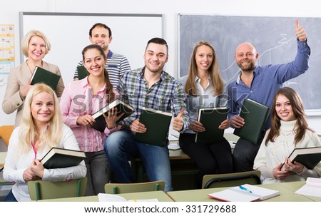 Smiling female professor and cheerful students posing in classroom at extension courses