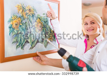 Smiling woman and man hanging art picture in frame on the wall. Focus on woman