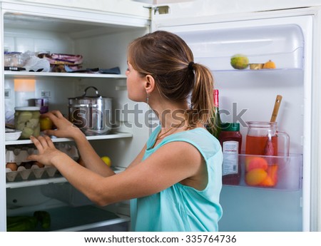 Young woman standing near refrigerator filled with products