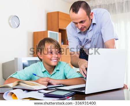 Positive adult man and smiling teenager boy studying with laptop indoors