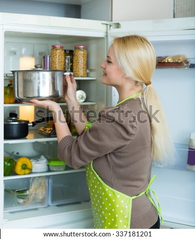 Blonde russian girl looking for something in fridge at home kitchen