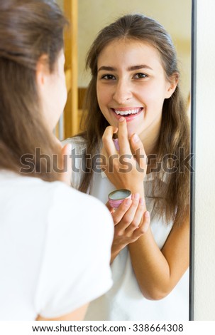 Smiling girl looks in the mirror and uses lip balm