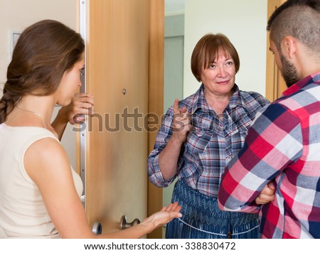 Young family arguing with displeased elderly female neighbor in the doorway
