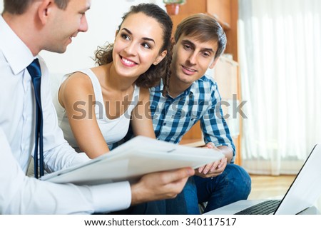 Positive sales consultant with laptop explaining young couple conditions of purchase