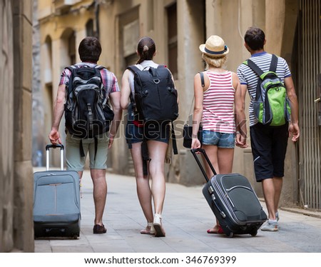 Two traveler couples with travel bags walking through the city. Back view