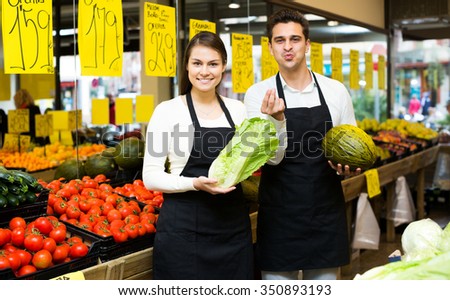 Young beautiful sellers offering good price for vegetables and fruits in his shop . Focus on the woman