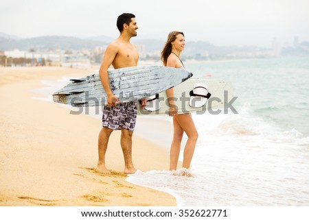 Cheerful young couple running on the beach with surf boards. Focus on the man