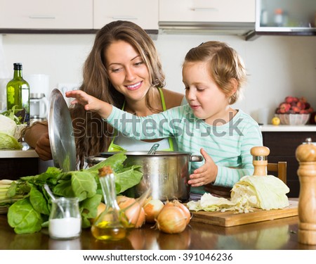 Happy young woman with little daughter cooking with vegetables at home kitchen