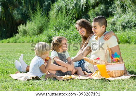 Happy young family of four having picnic at meadow at summer day