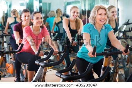 Positive females of different age training on exercise bikes together in modern fitness club