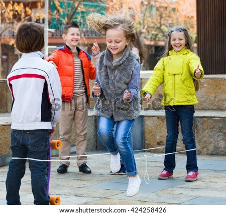 Smiling positive girl jumping while jump rope game with friends outdoor